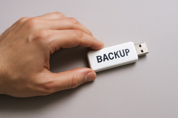A carefully holds a USB drive on a smooth light gray background symbolizing secure data protection and digital backup processes