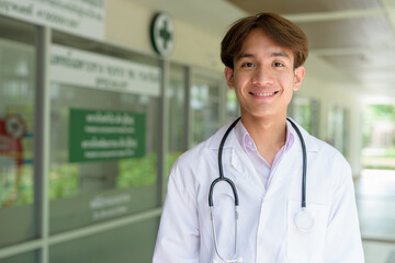 Young happy healthcare worker smiling and wearing lab coat in front of medical clinic