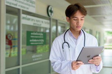 Young healthcare worker wearing lab coat in front of medical clinic using tablet computer