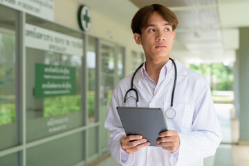 Young healthcare worker wearing lab coat in front of medical clinic using tablet computer