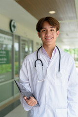 Young happy healthcare worker smiling and wearing lab coat in front of medical clinic