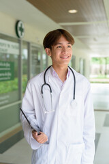 Young healthcare worker wearing lab coat in front of medical clinic thinking