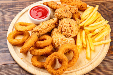 Chicken fillets, wings, onion rings and fries on  wooden background