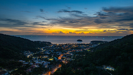 A breathtaking sunset paints the sky in vivid hues of orange and blue over a coastal town, with...