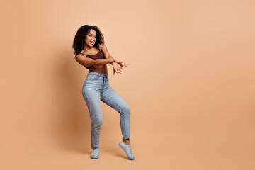 Joyful young woman dancing in casual attire on a beige background representing stylish and cheerful...