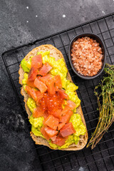 Toast with salty salmon, trout slices, avocado and red caviar. black background. top view