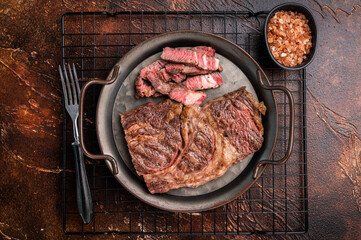 BBQ fried and sliced Chuck eye roll steak in a steel tray, prime beef meat. brown background. top view