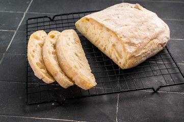 Fresh baked and sliced ciabatta bread on a rack. black background. top view