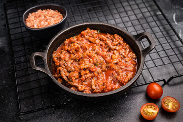 Bolognese sauce with minced beef, tomato paste and herbs in a skillet. black background. top view