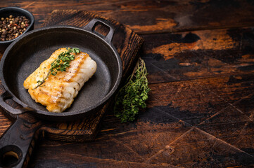 Roasted cod fish loin fiilet in skillet. Wooden background. top view