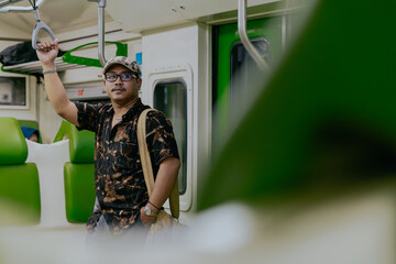 Asian man standing while holding a handle by train mrt or public transportation. Traveler man in a...