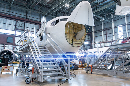 Front view of the white passenger airliner under maintenance in the aircraft hangar. The plane has opened weather radar. Checking mechanical systems for flight operations