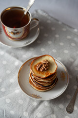 Stack of golden pancakes with walnuts and syrup on ceramic plate. Vintage tea set in background. Cozy morning breakfast scene.