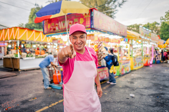 Portrait of a charismatic vendor selling his wares at a local fair in Latin America. The man is wearing pink clothing, with a food stand behind him.