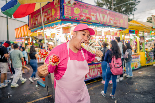 Portrait of a charismatic vendor selling his wares at a local fair in Latin America. The man is wearing pink clothing, with a food stand behind him.