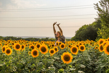 young blond woman standing in sunflowers on a field, raised her hands up, smiling, satisfied, 
view...