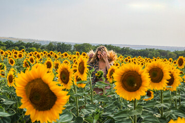young blond woman among sunflowers in a field, straightens her hair with her hands, 
view from...