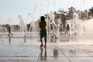 Children playing among the stream of water pouring from the park's floor fountain in the summer
