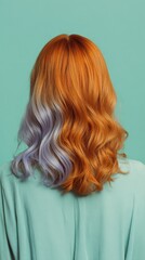 A person with long, wavy hair dyed half orange and half lavender, wearing a light green top, poses against a teal background.