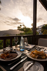 A table with two plates of food and two wine glasses. The table is set for two people and the mood is relaxed and intimate