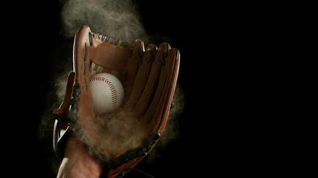 Super slow motion of hand in brown leather baseball glove caught ball isolated on black background . Filmed on high speed cinematic camera