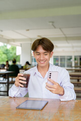 Non binary university student sitting in college campus using phone