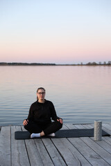 Woman practicing yoga on a wooden pier by the water at sunrise. Peaceful atmosphere, healthy...