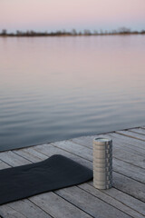 Yoga mat and massage roller on a wooden pier by the lake at sunrise. Concept of calm, wellness, and...