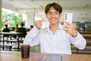 Non binary university student sitting in college campus using phone