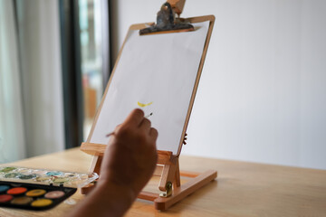 Artist painting on a canvas inside a cozy wooden interior with tools and a table nearby