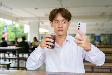 Non binary university student sitting in college campus using phone