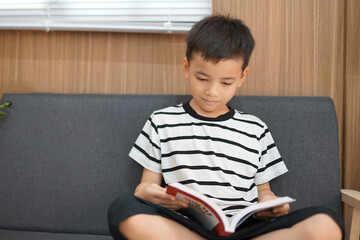 Young boy sitting on the floor smiling while reading a book at home
