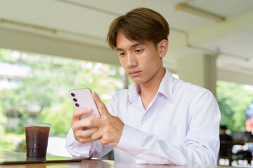 Non binary university student sitting in college campus using phone