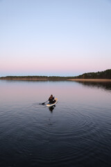 Young woman sitting on a paddleboard in the middle of a calm lake at sunset. Peaceful water...