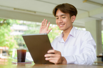Non binary university student sitting in college campus using tablet computer
