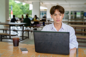 Non binary university student sitting in college campus using laptop computer