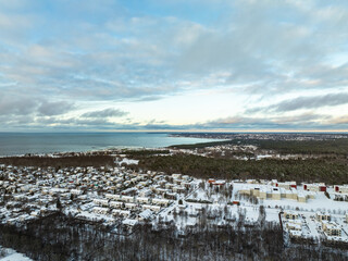 Aerial winter view of Pirita district in Tallinn, Estonia. Snow-covered houses, pine forests, and the Baltic Sea under a dramatic sky create a peaceful, scenic Nordic coastal landscape