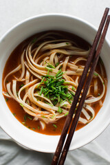 Overhead view of spicy noodle soup in a white bowl, top view of noodles in a spicy broth with...