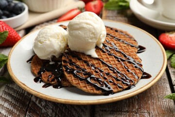 Tasty Dutch waffles (stroopwafels) with ice cream and chocolate sauce on wooden table, closeup