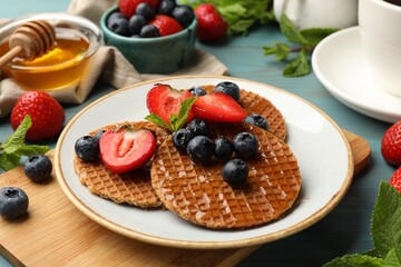 Tasty Dutch waffles (stroopwafels) with honey, berries and mint on light blue wooden table, closeup