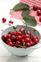 Fresh wet cherries in colander on white wooden table, closeup