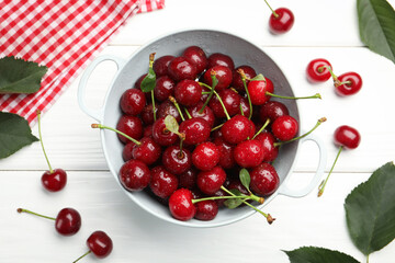 Fresh wet cherries in colander and leaves on white wooden table, flat lay