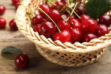 Fresh wet cherries in wicker basket on wooden table, closeup