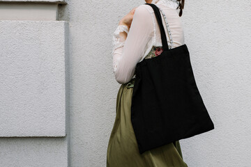 Young white woman holding black eco bag on arm shoulder or hand, street wall at background. city...