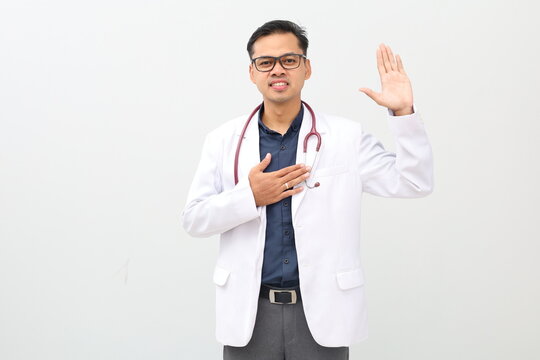 Adult asian man wearing doctor suit and stethoscope swearing with hand on chest and open palm, making a loyalty promise oath