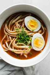 Overhead view of spicy noodle soup with eggs in a white bowl, top view of noodles eggs in a spicy broth with scallions