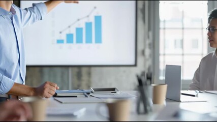 Business Presentation: A dynamic business professional illustrates rising trends on a screen for colleagues, fostering collaboration and strategic discussions within a modern office environment. - Powered by Adobe