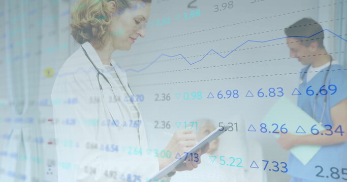 Female doctor with stethoscope reviewing tablet in ward, nurse consulting patient with folder