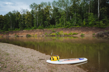 A bright and colorful paddle board is resting on the warm, sandy shore of the lake, eagerly waiting...