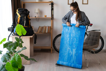Female hiker preparing to travel packing Hiking backpack with mat to trek in mountains in home...